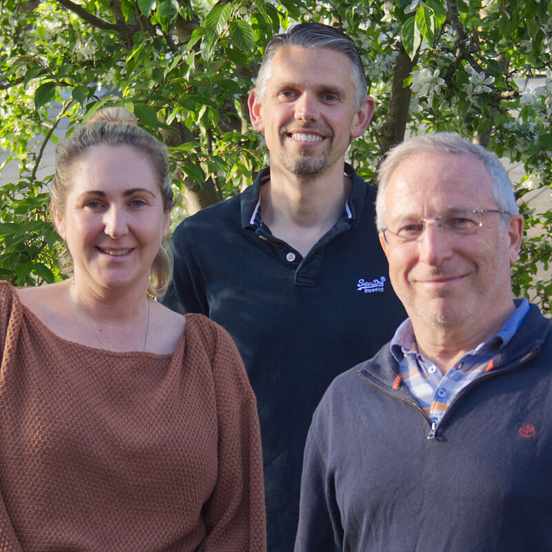 The smiling Bushey St James ward team of Mia Handley, Miles Ponder and Chris Shenton are standing together. The spring green leaves of a tree are behind them.