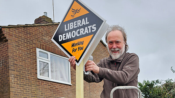 Retired Lib Dem councillor Jerry Evans is up a ladder installing a Lib Dem garden posterboard
