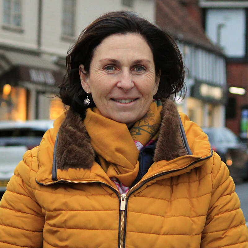 Emma Matanle in a yellow puffer jacket and scarf, stands on the High Street in Bushey Village