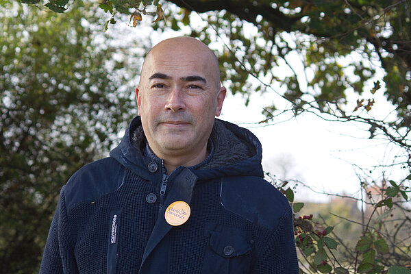 Councillor Paul Richards in a blue coat with a yellow Lib Dem badge, stands in front of leafy trees. Royal Connaught Park is just off in the distance